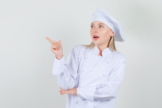 Chef mujer señalando con el dedo en uniforme blanco y mirando positivo