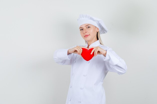 Chef mujer sosteniendo corazón rojo y sonriendo en uniforme blanco