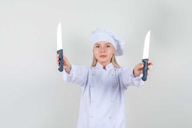 Chef mujer sosteniendo cuchillos y sonriendo en uniforme blanco