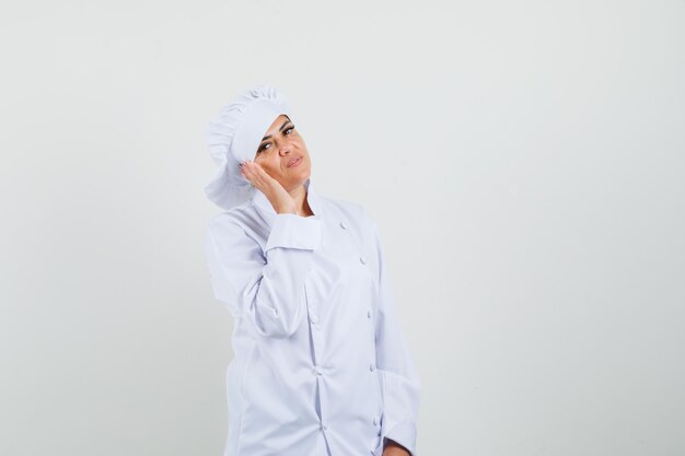 Chef mujer sosteniendo la mano cerca de la mejilla en uniforme blanco y mirando confiado