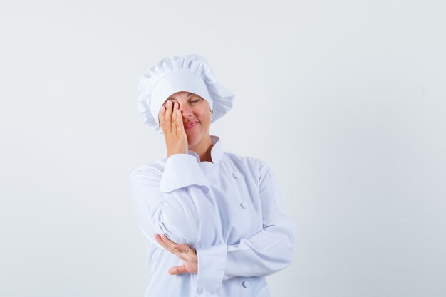 Chef mujer sosteniendo la mano en el ojo en uniforme blanco y mirando soñadora