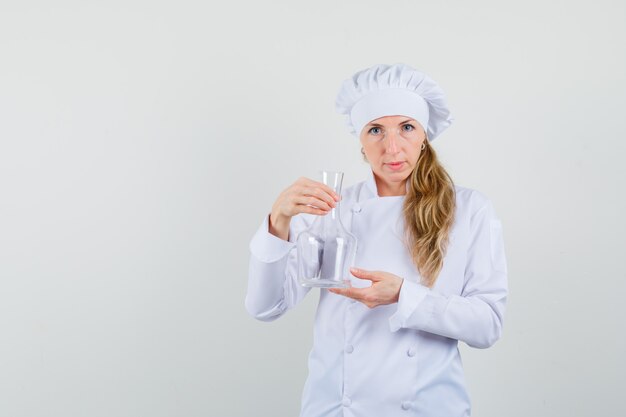 Chef mujer sosteniendo matraz químico en uniforme blanco