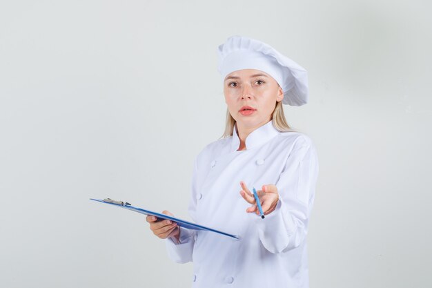 Chef mujer sosteniendo el portapapeles con lápiz en uniforme blanco y mirando confundido