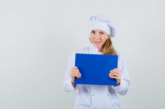 Chef mujer sosteniendo portapapeles en uniforme blanco y mirando confiado