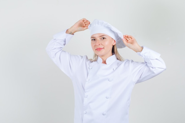 Chef mujer sosteniendo su sombrero en uniforme blanco y mirando alegre