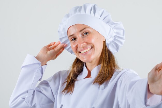Chef mujer sosteniendo su sombrero en uniforme blanco y mirando alegre
