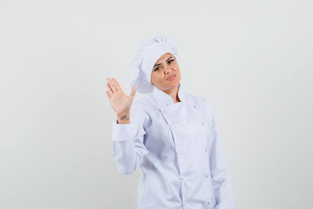 Chef mujer en uniforme blanco agitando la mano para saludar y mirar confiado