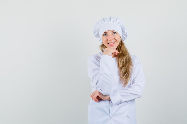 Chef mujer en uniforme blanco apoyando la barbilla en la mano y mirando feliz