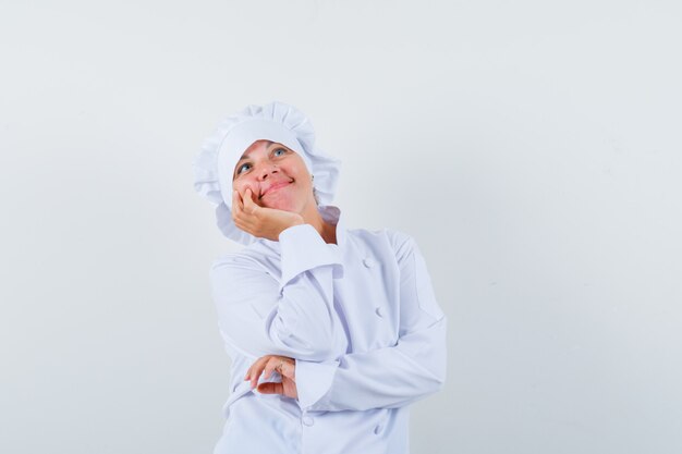 Chef mujer en uniforme blanco apoyando la barbilla en la palma y mirando soñadora