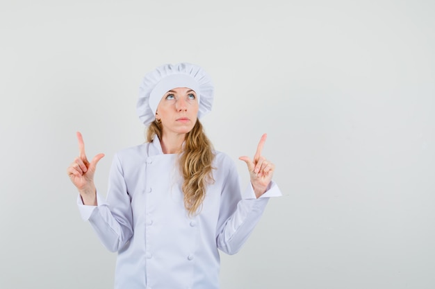 Chef mujer en uniforme blanco apuntando hacia arriba y mirando enfocado