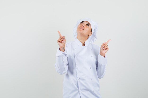 Chef mujer en uniforme blanco apuntando hacia arriba y mirando enfocado