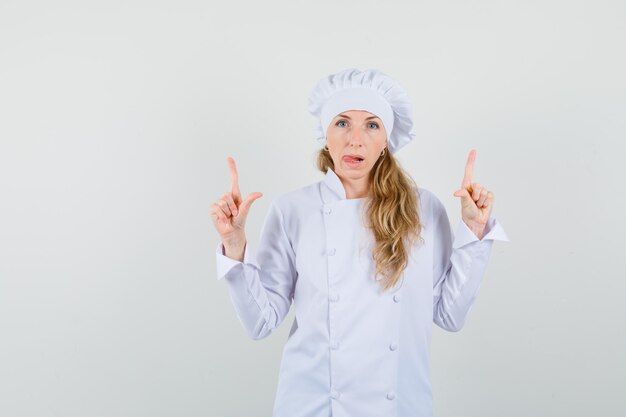 Chef mujer en uniforme blanco apuntando hacia arriba y sacando la lengua