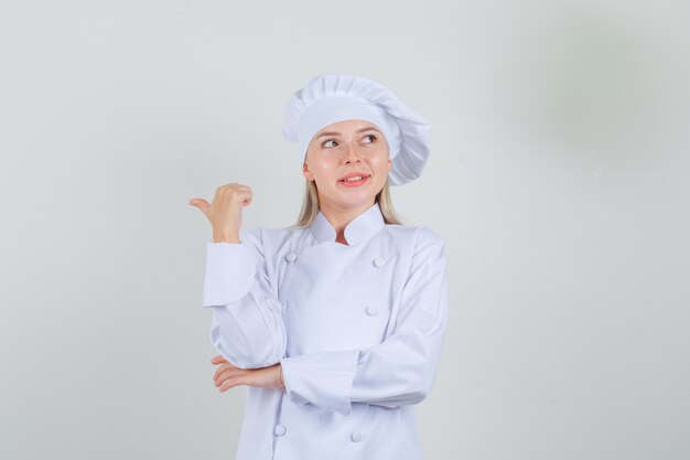 Chef mujer en uniforme blanco apuntando hacia atrás con el pulgar y sonriendo