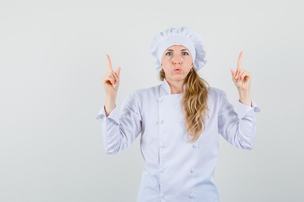 Chef mujer en uniforme blanco apuntando con el dedo hacia arriba y mirando esperanzado