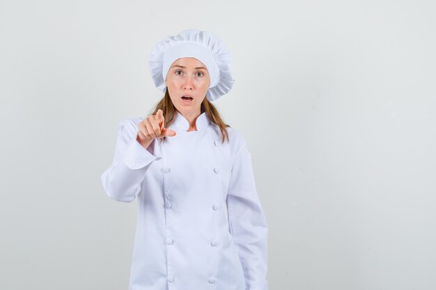 Chef mujer en uniforme blanco apuntando con el dedo y mirando sorprendido