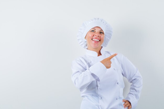 Chef mujer en uniforme blanco apuntando a la esquina superior derecha y mirando alegre