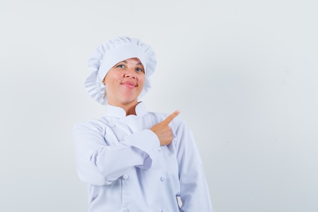 Chef mujer en uniforme blanco apuntando a la esquina superior derecha y mirando confiado