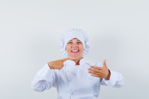 Chef mujer en uniforme blanco apuntando a un lado, fingiendo sostener algo y luciendo confiado