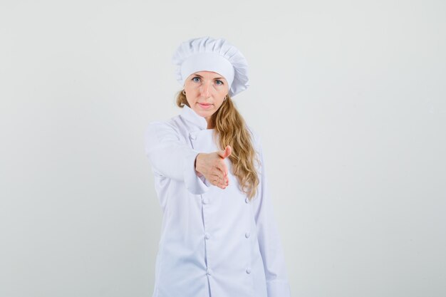 Chef mujer en uniforme blanco dando su mano para apretón de manos y mirando suave