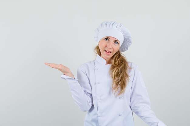 Chef mujer en uniforme blanco extendiendo la palma a un lado y mirando alegre