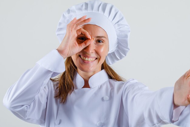 Chef mujer en uniforme blanco haciendo bien firmar en los ojos y mirando alegre