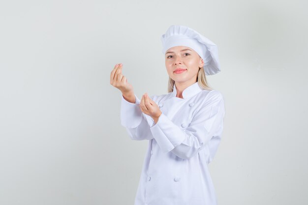 Chef mujer en uniforme blanco haciendo gesto de dinero y sonriendo