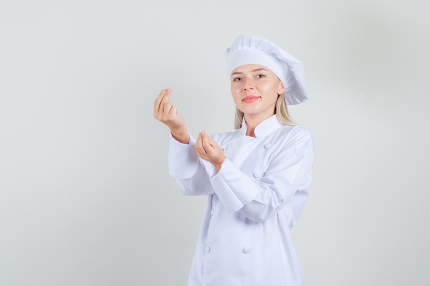 Chef mujer en uniforme blanco haciendo gesto de dinero y sonriendo