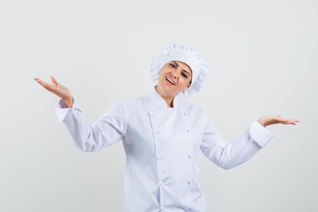 Chef mujer en uniforme blanco haciendo gesto de escalas y mirando contento