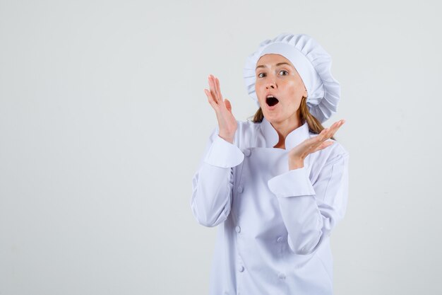 Chef mujer en uniforme blanco levantando las palmas abiertas y luciendo optimista