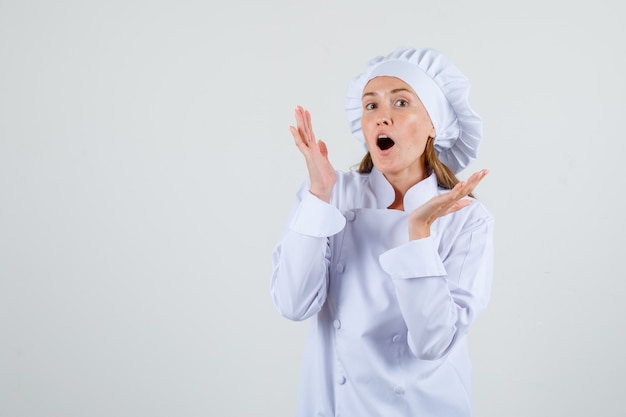 Chef mujer en uniforme blanco levantando las palmas abiertas y luciendo optimista