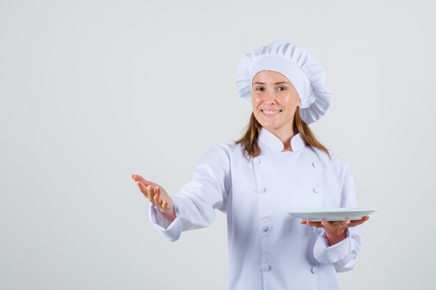 Chef mujer en uniforme blanco mostrando algo mientras sostiene la placa y mirando contento