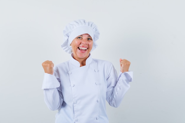 Chef mujer en uniforme blanco mostrando gesto ganador y mirando alegre