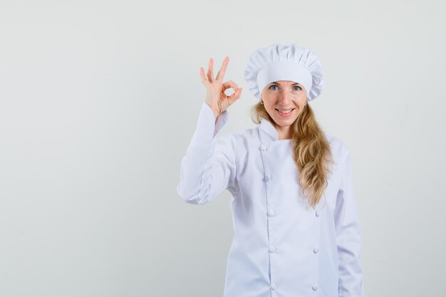 Chef mujer en uniforme blanco mostrando gesto ok y mirando alegre