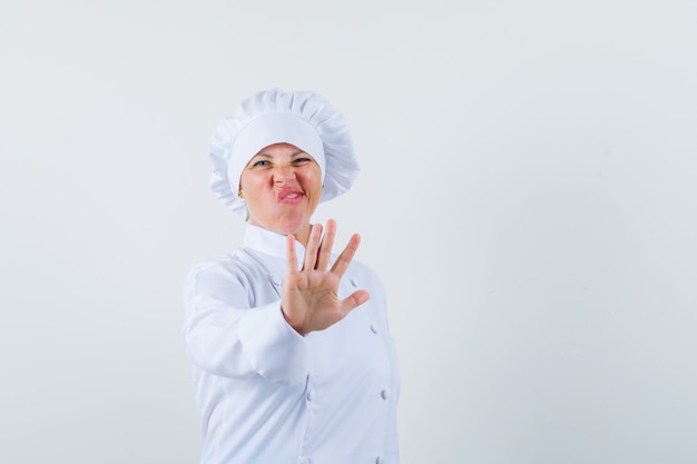 Chef mujer en uniforme blanco mostrando gesto de parada y mirando aburrido