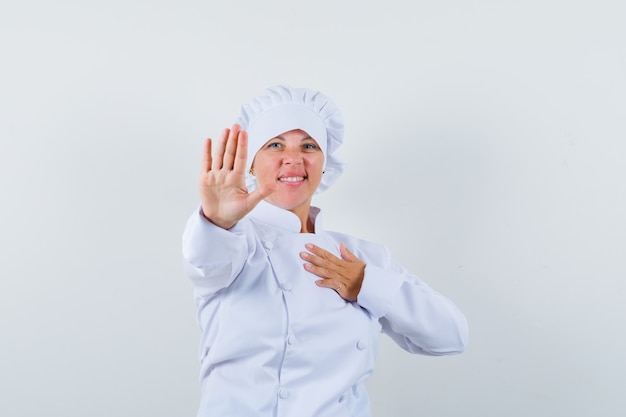 Chef mujer en uniforme blanco mostrando gesto de parada y mirando confiado