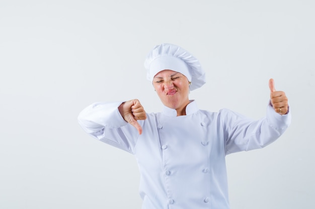 Foto gratuita chef mujer en uniforme blanco mostrando el pulgar hacia arriba y hacia abajo y mirando vacilante