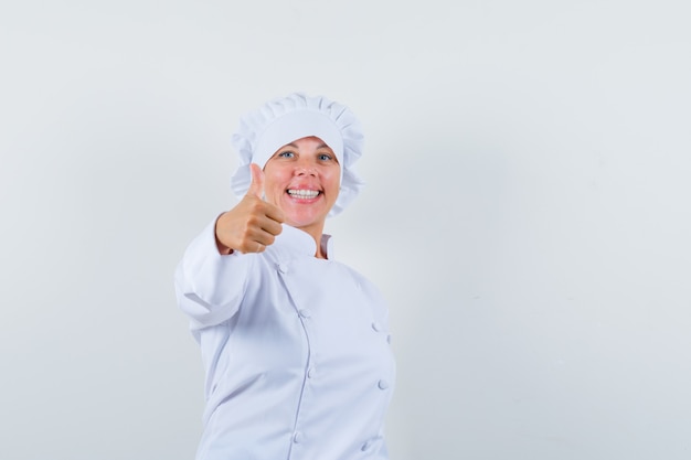 Chef mujer en uniforme blanco mostrando el pulgar hacia arriba y mirando feliz