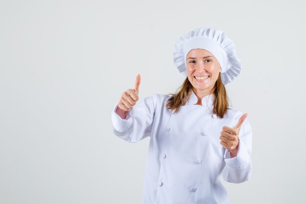 Chef mujer en uniforme blanco mostrando los pulgares hacia arriba y mirando contento