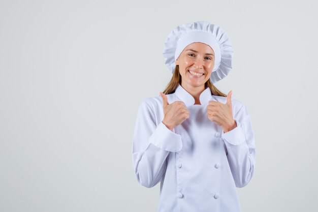 Chef mujer en uniforme blanco mostrando los pulgares hacia arriba y mirando feliz