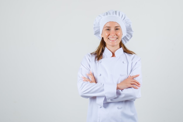 Foto gratuita chef mujer en uniforme blanco de pie con los brazos cruzados y mirando alegre