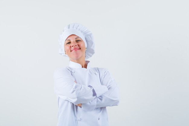 Chef mujer en uniforme blanco de pie con los brazos cruzados y mirando seguro de sí mismo