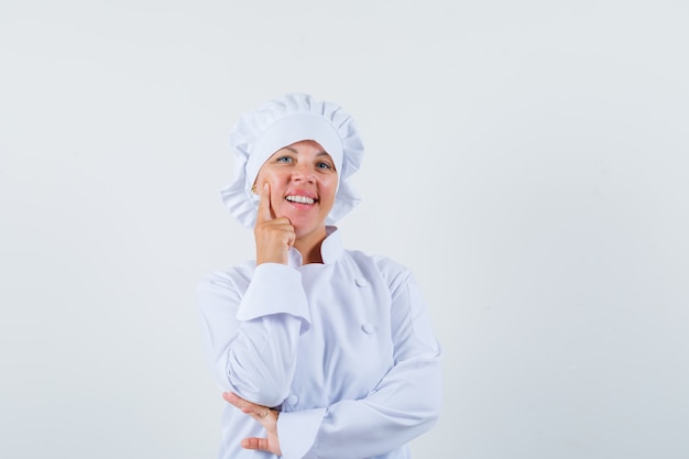 Chef mujer en uniforme blanco de pie en pose de pensamiento y mirando optimista