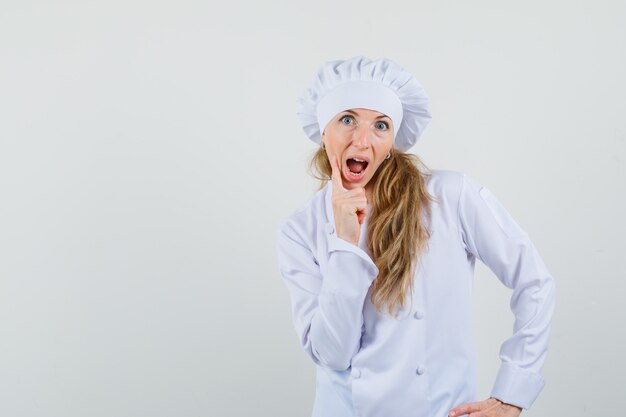 Chef mujer en uniforme blanco de pie en pose de pensamiento y mirando sorprendido