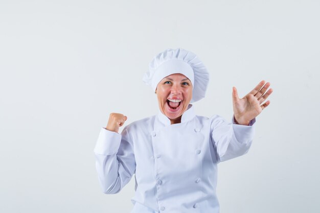 Chef mujer en uniforme blanco posando como mostrando su nueva receta de comida y luciendo optimista