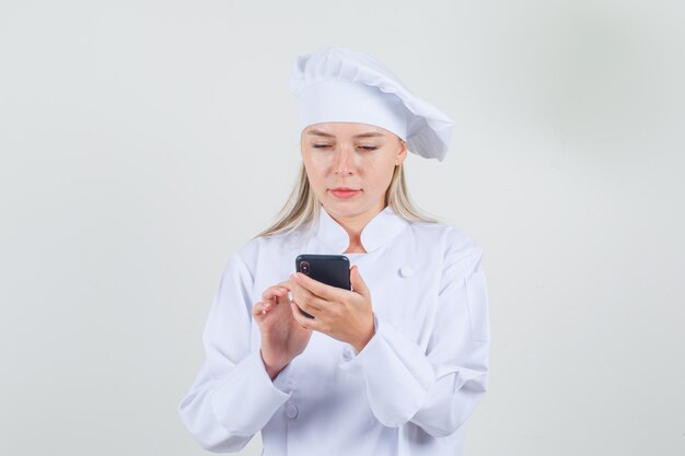 Chef mujer en uniforme blanco con smartphone y mirando ocupado