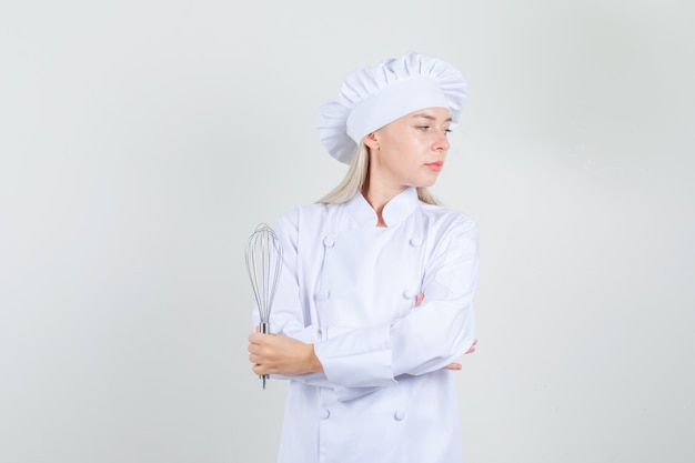 Chef mujer en uniforme blanco sosteniendo batidor y mirando a un lado