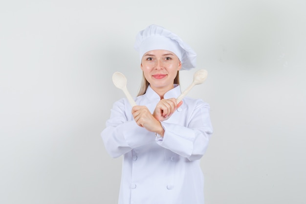 Chef mujer en uniforme blanco sosteniendo cucharas de madera y mirando alegre