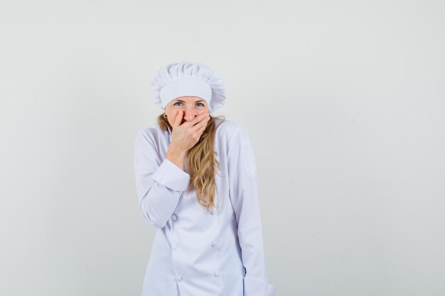 Chef mujer en uniforme blanco sosteniendo la mano en la boca mientras se ríe