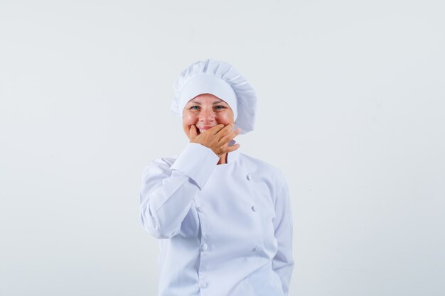 Chef mujer en uniforme blanco sosteniendo la mano sobre sus dientes y mirando alegre