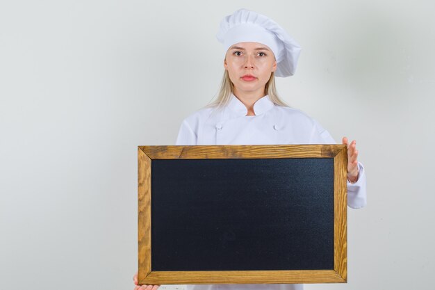 Chef mujer en uniforme blanco sosteniendo la pizarra y mirando seria